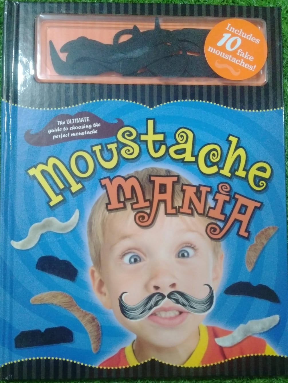 Book titled 'Moustache Mania' with a child's face on the cover, featuring fake moustaches.