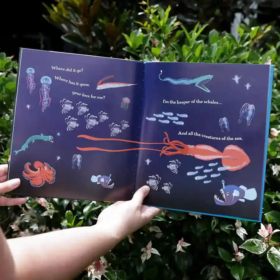 Open book with underwater illustrations held by a person against a green leafy background